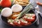 Sliced tomatoes with cheese and herbs in a black plate with onions, sweet peppers, eggs and french fries.