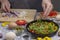 Sliced tomatoes and greens in a pan. Hands chop onion