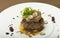 Sliced truffles topped on a grilled steak,  beef and pork,  with vegetable and sauce,  on a white plate,  brown background