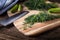 Sliced twig of dill on a wooden board with cucumber, kknife and