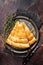 Slices of baked Round Borek cheese pie in kitchen tray with herbs. Dark background. Top view