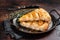 Slices of baked Round Borek cheese pie in kitchen tray with herbs. Dark background. Top view. Copy space