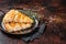 Slices of baked Round Borek cheese pie in kitchen tray with herbs. Dark background. Top view. Copy space