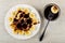 Slices of banana poured chocolate sauce in plate, slice of banana on fork above bowl on wooden table. Top view