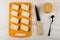 Slices of bread on cutting board, knife, bowl with peanut butter, spoon on wooden table. Top view