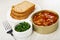 Slices of bread, fork in plate, opened jar with sprat in tomato sauce, fork, bowl with chopped parsley on wooden table