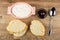 Slices of bread, pink bowl with soft cottage cheese, bowl with chocolate sauce, spoon on table. Top view