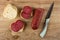 Slices of bread, sandwiches with smoked sausage, knife, piece of sausage on wooden table. Top view