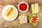 Slices of cheese in plate, bowl with sweet pepper, slice of bread, sandwiches with cheese, lettuce and pepper on table. Top view