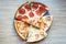 Slices of different pizza with bacon, pepperoni sausages, mushrooms and cheese on a plate and a wooden background. Top view