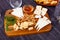 Slices of four varieties of cheeses on wooden board with honey, walnuts, greens