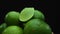 Slices of fresh lime are arranged in a pile with a black background. Comestible.