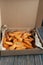 Slices of fried potatoes in box for food delivery. Delivered take away fast food on wooden background
