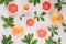 Slices grapefruit and green leaves on soft white wooden background, pattern, top view.
