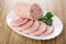 Slices of ham sausage, parsley in white dish on wooden table