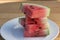 Slices of Organic California grown Watermelon stacked on a white plate on a wooden table.