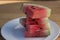 Slices of Organic California grown Watermelon stacked on a white plate on a wooden table.