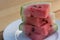 Slices of Organic California grown Watermelon stacked on a white plate on a wooden table.