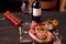 slices of raw rack of lamb on a cutting board with peppercorns, olive oil, cherry tomatoes on a twig, garlic and red chili peppers