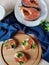 Slices of red fish homemade salt on a white plate and sandwiches with her decorated with blue textiles