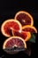 Slices of red sicilian orange fruit and green leaf on black reflective background