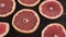 slices of red tasty grapefruit rotating on black wooden table close up view from top