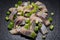 Slices of Salted Boneless wild-caught Atlantic Herring garnished with Chopped Green Onion Scallions. Black natural stone