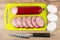 Slices of sausage on cutting board, chicken eggs and knife