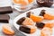 Slices of tangerine in chocolate served on a white plate, white wooden textured background.