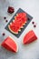 Slices of watermelon on the black plate, cherries and pieces of watermelon on the concrete background.