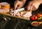 Slicing boiled sausage on a cutting board for preparing a salad. Knife in the hand of a cook on the kitchen table