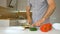 Slicing green bell pepper on wooden cutting board. Male hand cuts capsicum with knife. Man is cutting the sweet