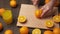 Slicing an orange on a kitchen cutting board, wooden table as background, close view. Glass of orange juice.