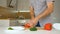 Slicing red bell pepper on wooden cutting board. Male hand cuts capsicum with knife. Man is cutting the sweet vegetables