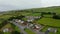 Slide and pan aerial shot of group of family houses in village. Green meadows and grasslands in slope behind. Ireland