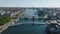 Slide and pan aerial view of pair of bridges over water canal in city. Modern design cyclist and pedestrian bridge and