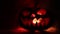 Slider shot. Scary Halloween pumpkin with carved eyes and a smile with burning candles inside on a dark background with fire and f