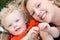 Slightly smiling toddler boy cuddles outdoors on blanket with pretty mommy.