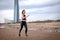 Slim athletic European girl in sportswear running on the sand on the beach against the background of the sky and a tall modern