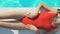 Slim attractive lady in red swimsuit lying near pool and sunbathing, sunscreen