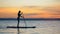 Slim attractive woman is moving on her paddleboard across the sunset waters