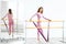 Slim ballerina woman girl in pink tracksuit. Stretching at ballet machine with resistance rubber. Athletic flexibility