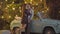 Slim beautiful woman coming to man standing at retro car with garlands shining at the background and hugging boyfriend