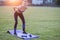 Slim blonde girl plays sports and performs yoga poses in summer grass covered stadium on a sunset background. Woman doing