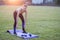 Slim blonde girl plays sports and performs yoga poses in summer grass covered stadium on a sunset background. Woman doing