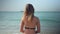 Slim blonde woman in bikini is sitting on a beach and watching horizon on sea in sunny day