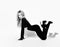 Slim blonde woman with pouty lips in tight black overall suit and high-heeled shoes stands on all fours sexy posing