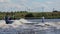 Slim boy playfully rides waterski at speed following motor boat along river