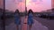 Slim brunette girl in blue dress walks on the street against pink sunset sky, 4K video