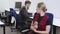 Slim charming young woman eating apple in office with blurred man messaging online at background. Portrait of positive